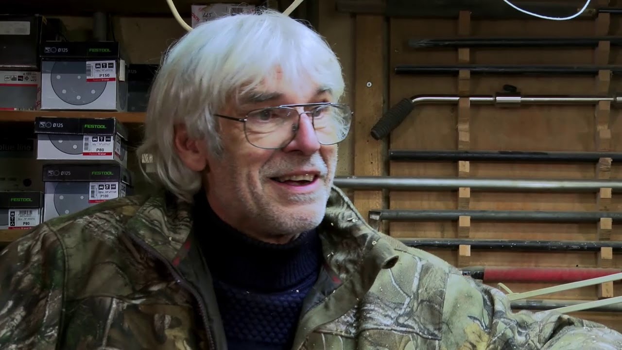 Hans-Henning Pedersen med hvidt hår og briller, mens han fortæller i værkstedet.